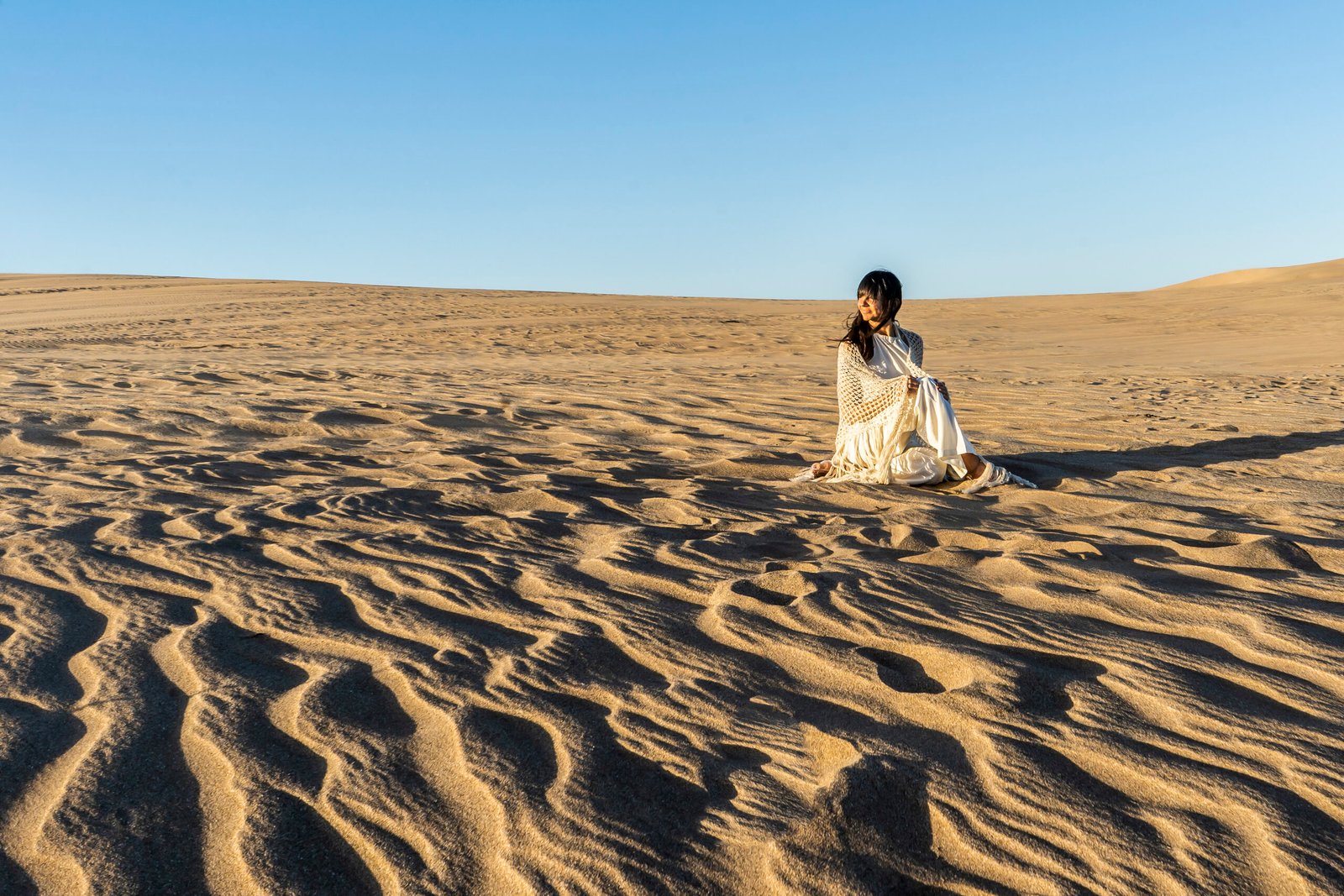 A woman dressed in white is watching the sunset on a dune in Dubai